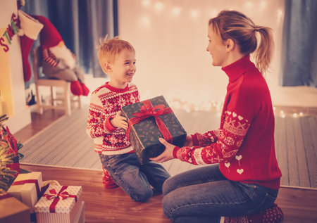 Mother and son indoors sitting on the floor and giving present box each other in Christmas eve.の写真素材
