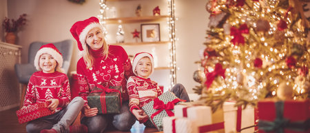 Mother and her son ad daughter sitting indoors with Christmas present boxes in their hands.の写真素材