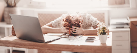 Tired woman putting her head on her hands on the desk in the officeの写真素材