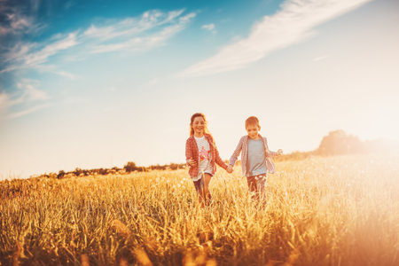 Two children running on the summer field by holding hands.の写真素材