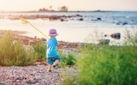 Child going to the water with net in his hand along pebble seaside.の写真素材