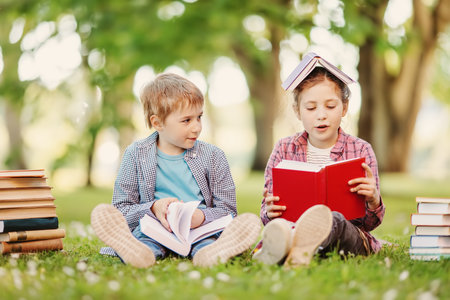 Boy and girl sitting on the meadow with books in their hands.の写真素材