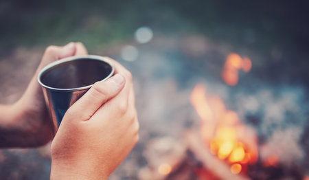 Humans hands holding the metal cup with hot drink above the fire.の写真素材