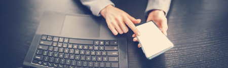 Woman holding in her hands mobile phone and typing on the laptop.の写真素材