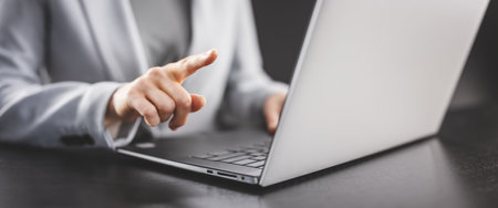Businesswoman sitting at the black table and pointing by finger on the display of her laptop.