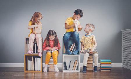 Group of children sitting on the books stacks and on the bookshelves in the room and reading periodical.の写真素材