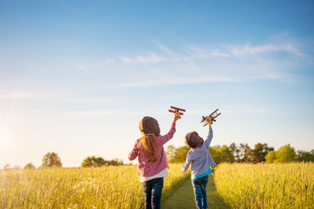 Boy and girl plaing with wooden planes on the field in sunsetの写真素材