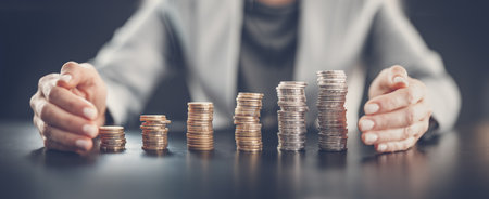 Woman sitting at the table and holding hands around the columns of coins.の写真素材