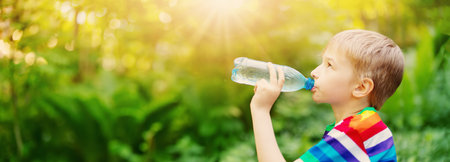 Boy standing in the natural park and drinking water from transparent bottle.の写真素材