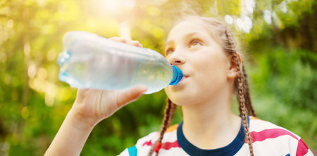 Girl standing in the natural park and drinking water from transparent bottle.の写真素材