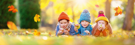 Children lying on the grass with apple in their hands in autumnal park.の写真素材