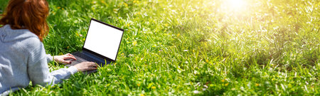Woman lying with laptop on the blossoming meadow in natural park.