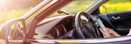 Woman sitting at the steering wheel and typing in smartphone.