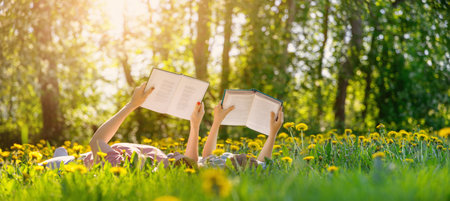 Mother and her child lying down on the green field with blooming flowers and reading books.の写真素材