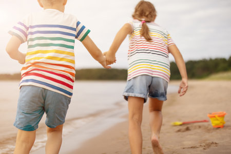 Boy and girl run by holding hands along waters edge of a sea.の写真素材