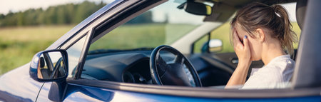 Young woman sitting behind the wheel and covering her face by hands.の写真素材