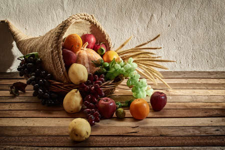 Thanksgiving cornucopia filled with pumpkins and fruit decorated with flower against a rustic wooden backgroundの写真素材