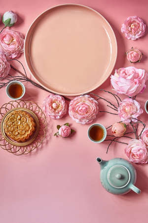 Mid autumn festival. Moon cake decorated with pink flower with teapot and cup of tea. Empty plate symbol of as moon.の写真素材