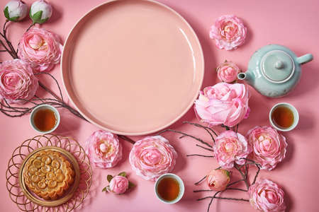 Mid autumn festival. Moon cake decorated with pink flower with teapot and cup of tea.Empty plate symbol of as moon.の写真素材