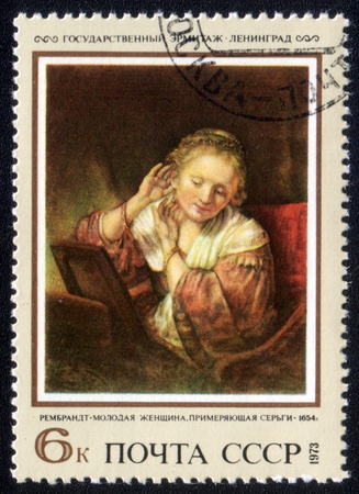 USSR - CIRCA 1973: A stamp printed in the USSR shows painting "Young woman trying earrings" by artist Rembrandt, stamp from collection Hermitage, circa 1973.のeditorial素材