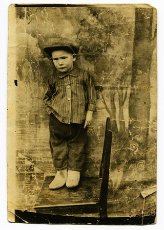 Ussr - CIRCA 1930s: An antique Black & White photo show little boy in a cap standing on a chairのeditorial素材