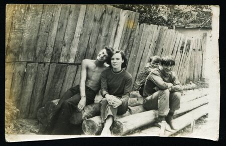 Ussr - CIRCA 1980s: An antique Black & White photo show young people sitting on the logs near the fenceのeditorial素材