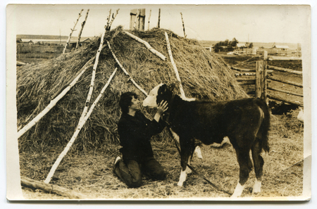 Ussr - CIRCA 1980s: An antique Black & White photo show A man kisses a kitten in the hayのeditorial素材