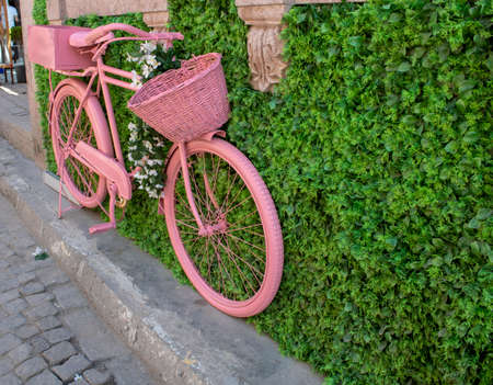 Old pink basket bike standing on pavement. It's attached to the wall.の写真素材