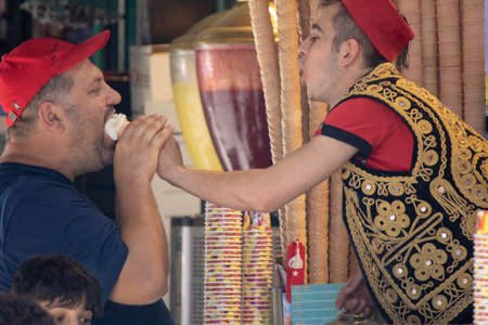 Istanbul, Turkey - August 19, 2019:Vendor in traditional dress feeding ice cream to customer
