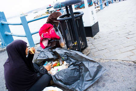Syrian woman wearing black burqa looking for food from garbage with her children. They escaped the war in Syria.のeditorial素材