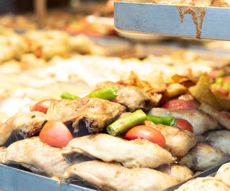 Roasted chicken legs. Peppers and tomatoes close-up. It was taken in front of the restaurant. There is glass in front.の写真素材