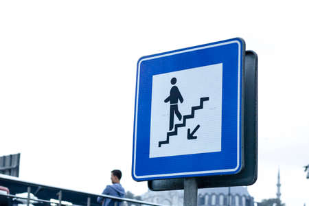 Street sign of man descending the stairs, white man on blue square, with blurred outdoor background