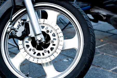 Closeup detail of a racing motorcycle's front wheel. This is the brake caliper, rotor, rim, tire,...