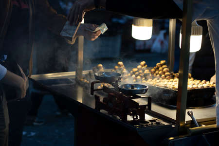 Man hanging the wheelbarrow with boiled corn and baked chestnuts. Photographed in the evening. The old scale is still standing.の写真素材