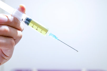 A syringe held in hand. It contains yellow liquid. Close-up and blurred background.の写真素材