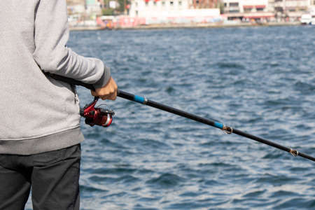 Man fishing by the sea. Close-up of fishing rod and reel. He holds it.の写真素材