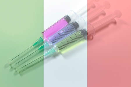 Three medical syringe with blue, green and red liquids. Italy flag in the background.の写真素材