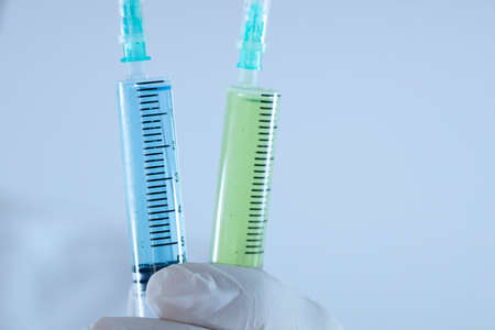 The doctor is holding the syringe with blue liquid in the glove. Syringe focused.の写真素材