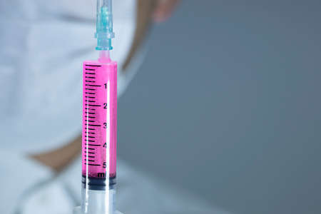 The doctor is holding the syringe with blue liquid in the glove. Close-up. Syringe focused. The doctor has a white outfit.の写真素材