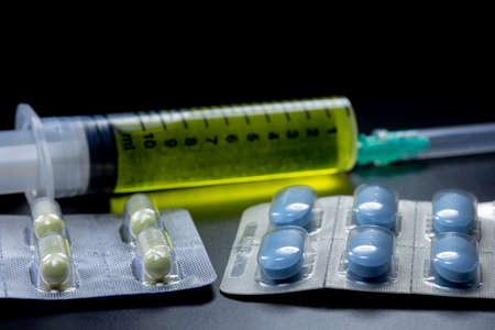Round pills and syringe with yellow liquid inside. Photographs were taken in the black background...