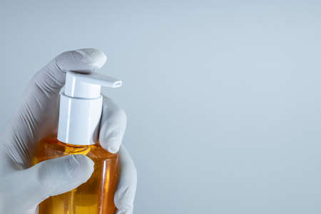Hand sanitizer against germs and viruses. Contains alcohol. A hand wearing a white glove is holding an orange bottle.の写真素材