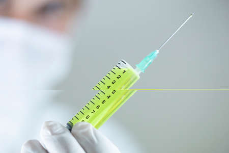 The doctor is holding one vaccines in his hand. Vaccines in yellow colors. Studio shooting. Close up.の写真素材