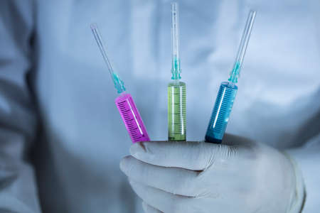 The doctor is holding three vaccines in his hand. Vaccines in red and green colors. Studio shooting. Close up.の写真素材