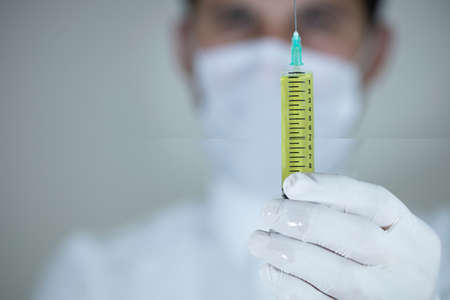 The doctor is holding one vaccines in his hand. Vaccines in yellow colors. Studio shooting. Close...