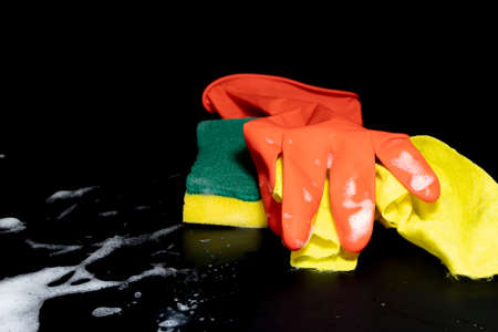 Scouring sponge foaming gloves and yellow cleaning cloth. In black background. Close up.