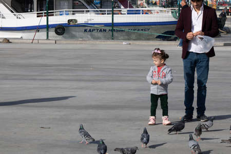 Istanbul, Turkey - November-07.2019: The young man walks his little sister. It feeds the pigeons. Filmed in clear sunny weather in winter.のeditorial素材