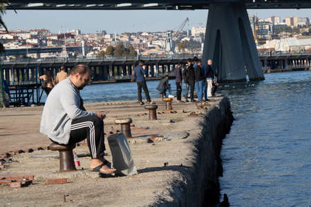 Istanbul, Turkey - November-02.2019: The man in a track suit and vest is sitting on a bitt. He is interested in his smart phone. A photo was taken on the edge of the Golden Horn.のeditorial素材