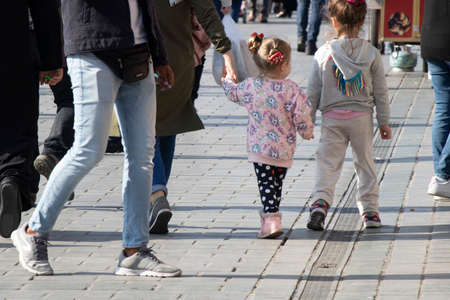 Istanbul, Turkey - October-27.2019: Big sister and little girl are walking hand in hand. Photographed from behind in the middle of the street. There are people around.のeditorial素材