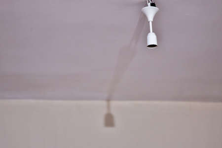 Bulb holder hanging on the ceiling. Empty is not plugged in. Its shadow is reflected on the wall.の写真素材