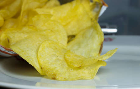 Opened chips bag and porcelain plate underneath. Plain potato chips are greasy.の写真素材